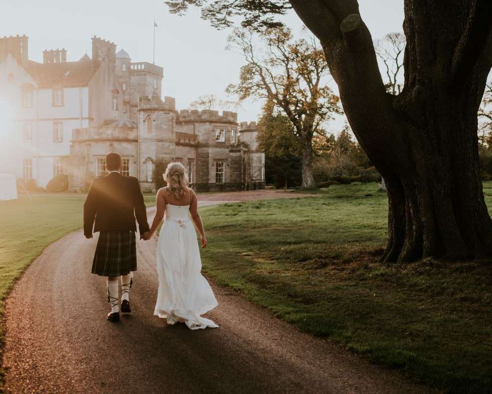 Bride and Groom in Golden Hour walking towards Castle. Winton Castle's Wedding Open Day